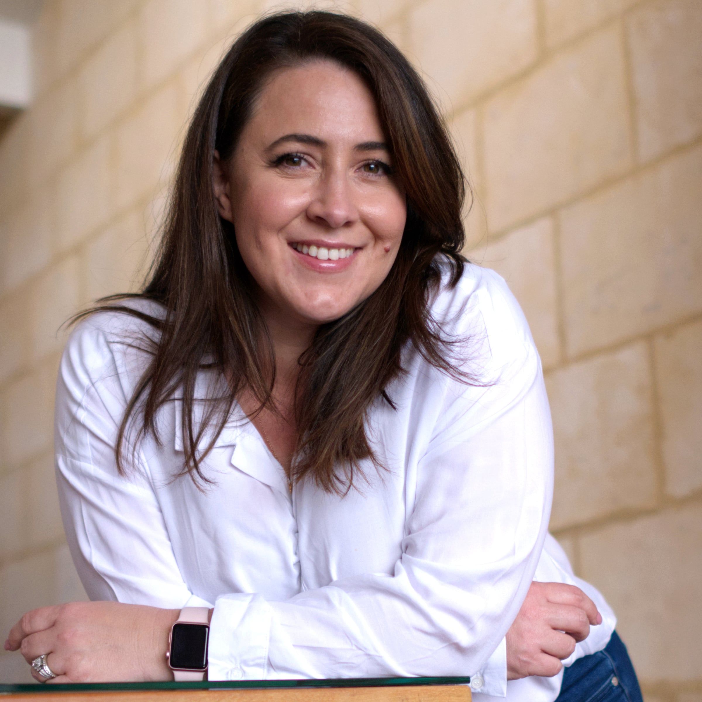Jessica Kidner smiling, in a white shirt against a sandstone wall
